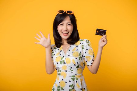Téléchargez les photos : Portrait asiatique jeune femme heureuse souriante en robe de printemps montrant carte de crédit en plastique isolé sur fond jaune. Paiement, argent et achat shopping concept de paiement. - en image libre de droit