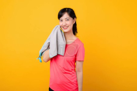 Téléchargez les photos : Portrait asiatique jeune sport fitness femme heureux sourire portant des vêtements de sport rose et serviette de visage faire de l'exercice séance d'entraînement sur fond jaune studio. bien-être et mode de vie sain concept. - en image libre de droit