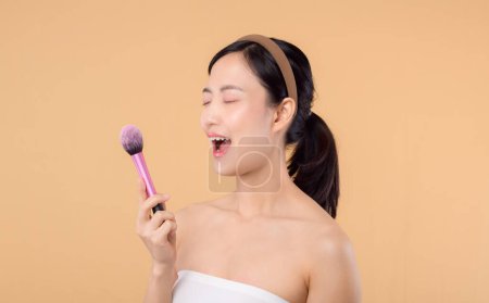 Photo for Portrait young happy asian woman with natural make up face holding cosmetic skin powder blusher isolated on beige background. Female apply skincare brush treatment. beauty product cosmetology concept. - Royalty Free Image