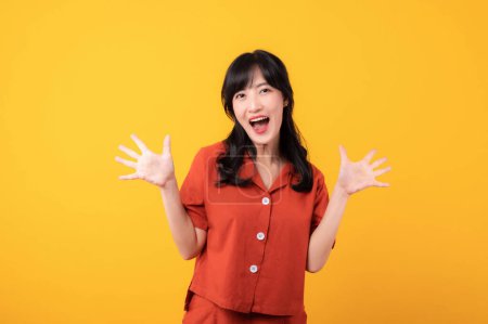 Téléchargez les photos : Portrait belle jeune femme asiatique heureux sourire habillé en vêtements orange regardant surpris, réagissant étonné, levant les sourcils impressionné isolé sur fond de studio jaune. - en image libre de droit