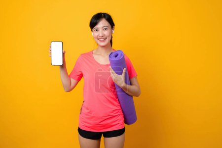 Téléchargez les photos : Portrait asiatique jeune sport fitness femme heureux sourire portant des vêtements de sport rose et smartphone faire de l'exercice séance d'entraînement sur fond jaune studio. technologie bien-être style de vie concept. - en image libre de droit