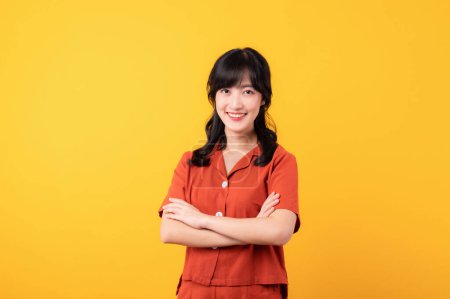 Téléchargez les photos : Portrait jeune réfléchi belle asiatique femme heureux sourire habillé en vêtements orange montrant geste de bras croisés isolé sur fond jaune studio. - en image libre de droit