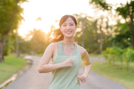Téléchargez les photos : S'adapter jeune femme asiatique jogging dans le parc souriant course heureuse et profiter d'un mode de vie sain en plein air. Joggeuse. Fitness fille coureuse dans le parc public. mode de vie sain et concept de bien-être - en image libre de droit