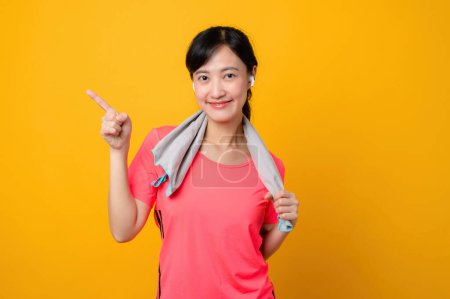 Téléchargez les photos : Portrait asiatique jeune sport fitness femme heureux sourire portant des vêtements de sport rose et serviette de visage faire de l'exercice séance d'entraînement sur fond jaune studio. bien-être et mode de vie sain concept. - en image libre de droit