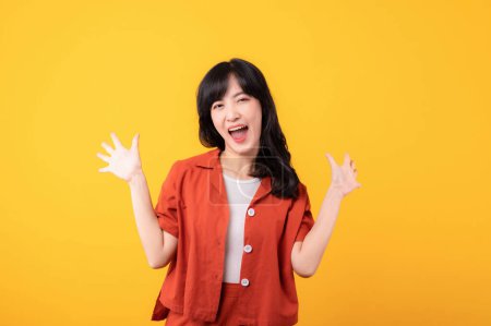 Foto de Retrato hermosa joven asiática mujer feliz sonrisa vestida con ropa naranja mostrando puño hasta gesto de la mano aislado en el fondo del estudio amarillo. Hurra con éxito celebrar el concepto de persona joven. - Imagen libre de derechos