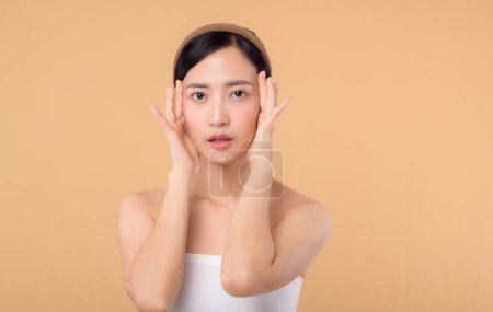 Téléchargez les photos : Belle asiatique fille modèle toucher frais lumineux hydraté peau du visage sur fond beige gros plan. Beauté visage jeune femme avec maquillage naturel et portrait de peau saine. Concept de soins de la peau - en image libre de droit