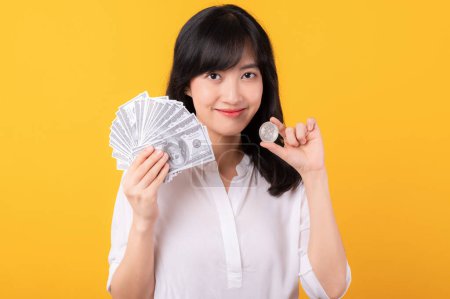 Photo for Portrait young beautiful asian woman enterpriser happy smile wearing white shirt and red plants holding cash dollar money and crypto digital currency isolation on yellow background. Wealth concept. - Royalty Free Image