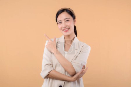 Téléchargez les photos : Studio portrait de heureux heureux heureux confiant jeune femme d'affaires asiatique. Belle jeune femme en veste blanche souriant à la caméra debout isolé sur fond de copyspace couleur beige uni - en image libre de droit
