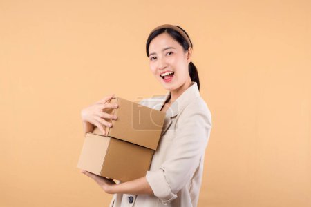 Photo for Portrait of successful happy confident young asian business woman wearing white jacket holding parcel box isolated on beige studio background, Delivery courier and shipping service concept. - Royalty Free Image