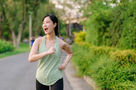 Foto de Ajuste joven mujer asiática corriendo en el parque sonriendo feliz corriendo y disfrutando de un estilo de vida saludable al aire libre. Una corredora. Chica corredor de fitness en el parque público. estilo de vida saludable y bienestar siendo concepto - Imagen libre de derechos