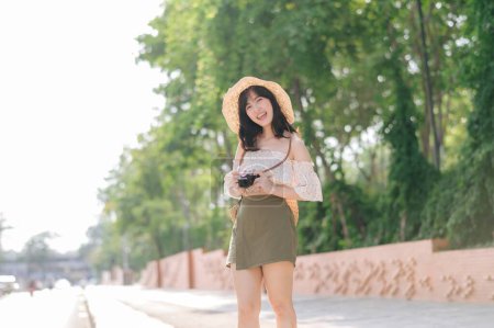 Foto de Retrato de mujer joven asiática viajero con sombrero de tejer y cesta y una cámara en verde parque público fondo de la naturaleza. Viaje viaje estilo de vida, viajero mundial o concepto de turismo de verano de Asia. - Imagen libre de derechos
