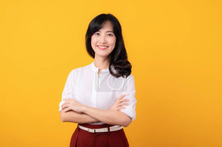 Foto de Retrato hermosa joven asiática mujer emprendedor feliz sonrisa vestida con camisa blanca y plantas rojas mostrando pensamiento gesto aislado en amarillo estudio fondo. - Imagen libre de derechos