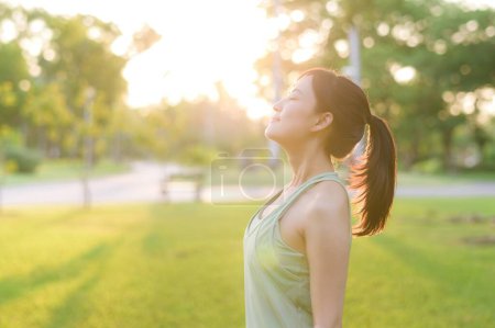 Foto de Una corredora. Ajuste mujer joven asiática con ropa deportiva verde respirando aire fresco en el parque antes de correr y disfrutar de un aire libre saludable. Chica corredor de fitness en el parque público. Bienestar siendo concepto - Imagen libre de derechos