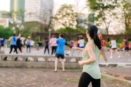 Photo for Female jogger. Fit Asian young woman with green sportswear aerobics dance exercise in park and enjoying a healthy outdoor. Fitness runner girl in public park. Wellness being concept - Royalty Free Image