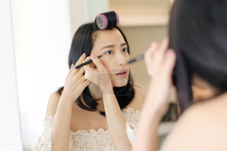 Téléchargez les photos : Belle jeune femme asiatique appliquant du maquillage devant le miroir. Concept de gens de style de vie. Publicité pour crème pour la peau, crème anti-rides, visage de bébé - en image libre de droit