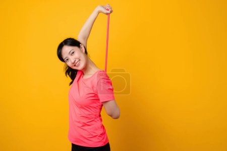 Téléchargez les photos : Portrait asiatique jeune femme de fitness sportive heureuse de porter des vêtements de sport roses et bande de résistance étirant faire de l'exercice séance d'entraînement sur fond jaune. bien-être mode de vie sain concept. - en image libre de droit