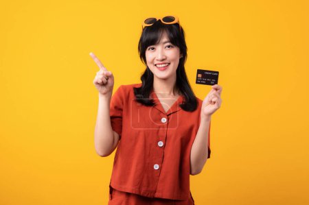 Photo for Portrait beautiful young asian woman happy smile dressed in orange clothes showing credit card and point finger to free space isolated on yellow background. Pay and purchase shopping payment concept. - Royalty Free Image