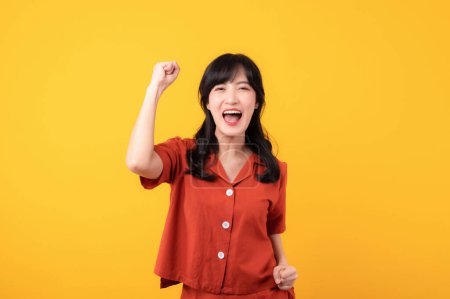 Photo for Portrait beautiful young asian woman happy smile dressed in orange clothes showing fist up hand gesture isolated on yellow studio background. Successful hooray celebrate young person concept. - Royalty Free Image