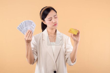Photo for Portrait of successful happy confident young asian business woman wearing white jacket holding cash money dollars and credit card standing over beige background. millionaire business, shopping concept - Royalty Free Image