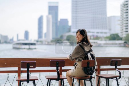 Téléchargez les photos : Jeune voyageuse asiatique sac à dos attendant un bateau express à quai sur la rivière Chao Phraya à Bangkok. Voyageur vérifiant les rues latérales. - en image libre de droit