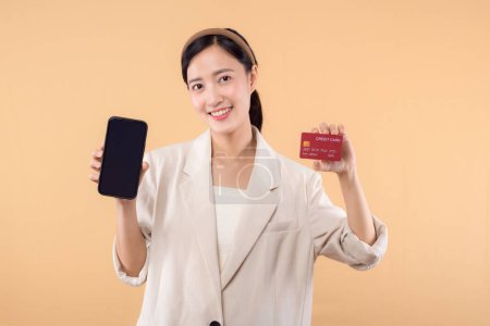Photo for Portrait of successful happy confident young asian business woman wearing white jacket holding smartphone and credit card standing over beige background. shopping concept. - Royalty Free Image