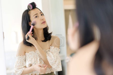 Téléchargez les photos : Belle jeune femme asiatique appliquant du maquillage devant le miroir. Concept de gens de style de vie. Publicité pour crème pour la peau, crème anti-rides, visage de bébé - en image libre de droit