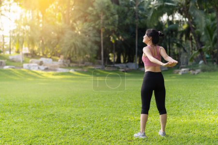 Foto de Una corredora. Inspírate en forma imagen activa de la joven asiática en ropa deportiva rosa estirando los músculos en el parque antes de correr, disfrutando de una actividad al aire libre saludable. Bienestar y fitness en un entorno natural. - Imagen libre de derechos