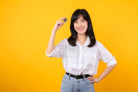 Photo for Discover the allure beautiful young Asian woman, dressed in white shirt and denim jeans, holding digital currency. Explore the evolving world of digital currencies in this stunning isolated portrait. - Royalty Free Image