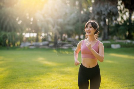 Photo for Female jogger. fit Asian young 30s woman wearing pink sportswear running in public park at sunset time, embodying the wellness concept and joy of fitness. - Royalty Free Image