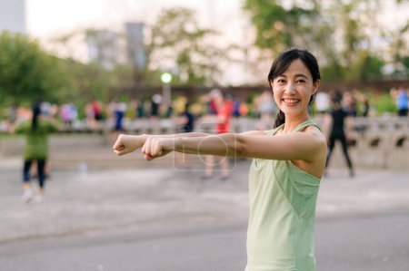 Photo for Female jogger. Fit Asian young woman with green sportswear aerobics dance exercise in park and enjoying a healthy outdoor. Fitness runner girl in public park. Wellness being concept - Royalty Free Image
