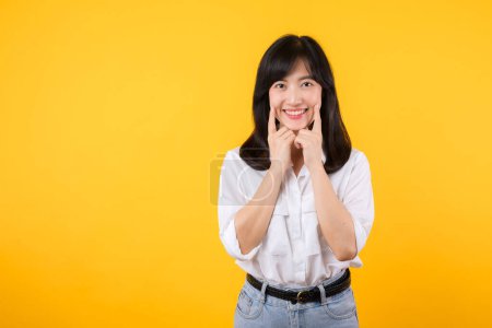 Téléchargez les photos : Jeune asiatique belle femme sourire heureux portant chemise blanche et des plantes de jean denim sur fond jaune isolé souriant montrant confiant et pointant avec les doigts dents et la bouche. Concept dentaire. - en image libre de droit