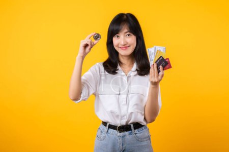 Photo for Capture the essence of digital currency with stunning portrait of Asian young woman confidently holds digital currency, cash, credit card, and smartphone. The digital currency concept. - Royalty Free Image