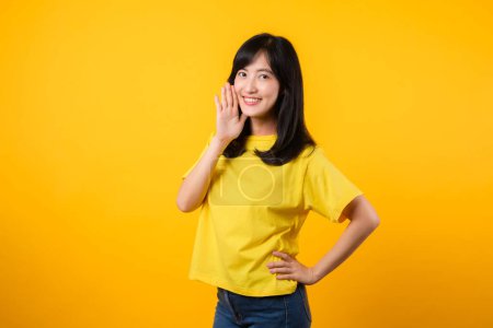 Photo for Experience the energy and expression in this vibrant portrait. young Asian woman wearing yellow t-shirt and denim jeans showcases dynamic shout hands gesture. Perfect for enthusiasm and excitement. - Royalty Free Image