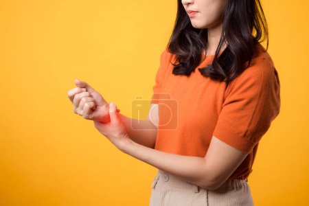 Téléchargez les photos : Asiatique jeune femme dans la trentaine avec blessure au poignet. tenant son poignet et regardant douloureux sur fond jaune. point de vue rapproché. blessure au poignet, douleur, inflammation et concept de soins médicaux. - en image libre de droit