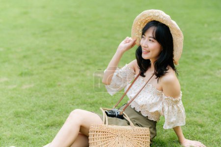 Foto de Retrato de mujer joven asiática viajero con sombrero de tejer y cesta y una cámara en verde parque público fondo de la naturaleza. Viaje viaje estilo de vida, viajero mundial o concepto de turismo de verano de Asia. - Imagen libre de derechos