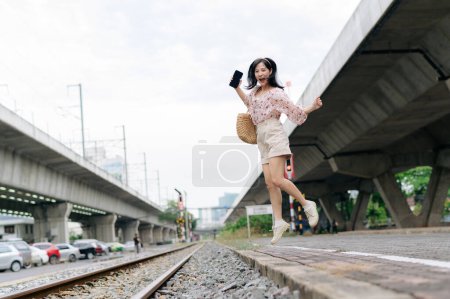 Téléchargez les photos : Jeune voyageuse asiatique sautant à côté de la gare ferroviaire de Bangkok. Voyage voyage style de vie, monde Voyage explorer ou Asie concept de tourisme d'été. - en image libre de droit