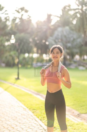 Foto de Fit sonrisa feliz 30s joven mujer asiática en ropa deportiva disfruta de refrescante puesta de sol correr en la naturaleza. La silueta de la figura contra el sol poniente es hermosa vista. Concepto de aptitud, salud o motivación. - Imagen libre de derechos