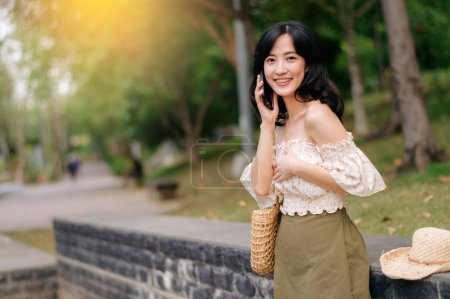 Photo for Portrait of young asian woman traveler with weaving hat, basket, mobile phone and camera on green public park background. Journey trip lifestyle, world travel explorer or Asia summer tourism concept. - Royalty Free Image