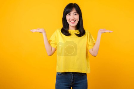 Téléchargez les photos : Attirez l'attention avec ce superbe portrait d'une jeune femme asiatique confiante. Elle porte un t-shirt jaune et un jean en denim, pointant vers l'espace libre. Parfait pour les projets créatifs. - en image libre de droit