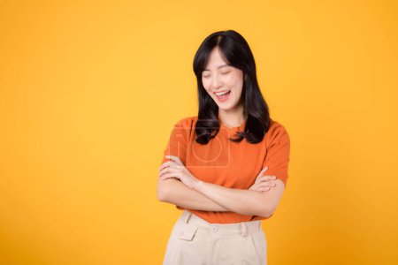 Téléchargez les photos : Jeune femme asiatique des années 30 portant une chemise orange montrant un geste de signe du bras croisé isolé sur fond jaune. Femme confiante avec geste mains concept. - en image libre de droit