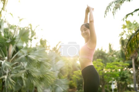 Téléchargez les photos : Forme jeune femme asiatique trentaine en rose vêtements de sport joue au yoga et étire les muscles. Adoptez un mode de vie sain en plein air avec la fille de yoga de fitness dans le parc public au coucher du soleil. concept bien-être et bien-être. - en image libre de droit