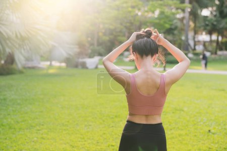 Téléchargez les photos : Mode de vie sain en plein air ajustement jeune femme asiatique trentaine en vêtements de sport rose prépare des exercices d'échauffement du corps dans le parc avant de courir. fitness fille coureuse au coucher du soleil. concept de bien-être et de bien-être. - en image libre de droit