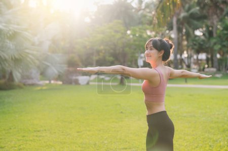 Téléchargez les photos : Mode de vie sain en plein air ajustement jeune femme asiatique trentaine en vêtements de sport rose prépare des exercices d'échauffement du corps dans le parc avant de courir. fitness fille coureuse au coucher du soleil. concept de bien-être et de bien-être. - en image libre de droit