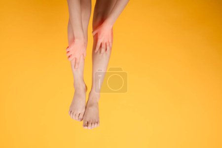 Téléchargez les photos : Un gros plan des jambes de la femme avec les mains tenant leurs jambes douloureuses sur fond jaune vif. Intégrer le concept de jambes santé. - en image libre de droit