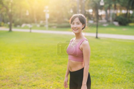 Foto de Experimenta la alegría de una corredora femenina feliz y en forma de los años 30. Mujer asiática vestida con ropa deportiva rosa, disfrutando del aire fresco en un parque público. Abrace la vida de bienestar y conéctese con la naturaleza. - Imagen libre de derechos