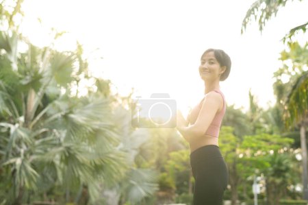 Téléchargez les photos : Bien-être et bien-être en forme jeune femme asiatique trentaine en tenue de sport rose s'engage dans le yoga et étire ses muscles. Adoptez un mode de vie sain en plein air avec une fille de yoga de fitness dans un parc public au coucher du soleil. - en image libre de droit