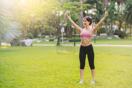 Photo for Embrace wellness living and nature with a happy, fit 30s Asian woman. Wearing pink sportswear, she breathes fresh air in a public park, embodying a healthy outdoor lifestyle - Royalty Free Image