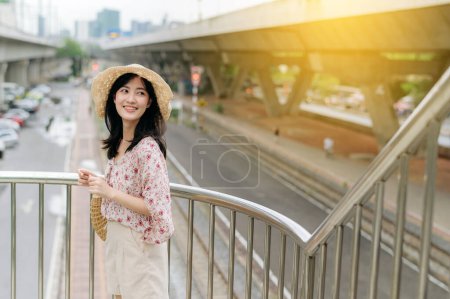 Téléchargez les photos : Asiatique jeune femme voyageur avec panier à tisser heureux sourire debout sur le passage supérieur avec fond ferroviaire. Voyage voyage style de vie, monde Voyage explorer ou Asie concept de tourisme d'été. - en image libre de droit