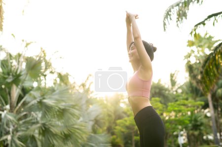 Photo for Embrace healthy outdoor lifestyle fit young Asian woman 30s in pink sportswear engages in yoga and stretches muscles in a public park at sunrise. concept of wellness and well-being fitness yoga girl. - Royalty Free Image
