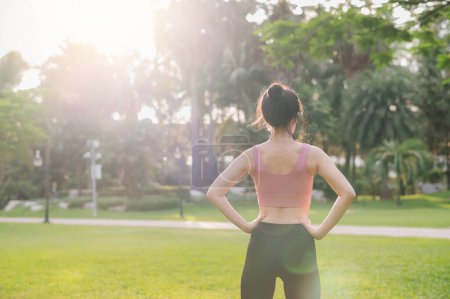 Photo for Embrace wellness living in nature as a happy, fit 30s Asian woman warms up her body in a public park before a sunset run, wearing pink sportswear. - Royalty Free Image
